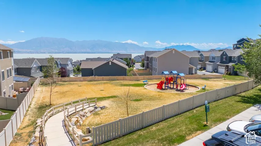 Community playground with a paved pathway, surrounded by fencing, and distant mountain scenery