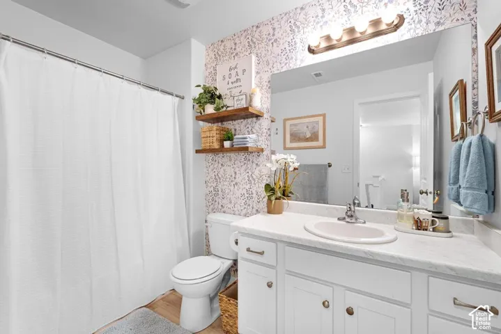 Vanity with white cabinetry and integrated sink, wall-mounted light fixture, full-width vanity mirror, and wood-finish flooring