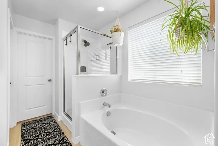 Recessed lighting, wood-finish flooring, built-in bathtub, glass-enclosed shower, and a white window blind