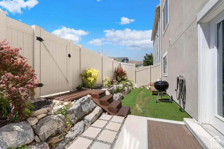 Paved patio with a stone retaining wall, artificial turf lawn, and vinyl fencing