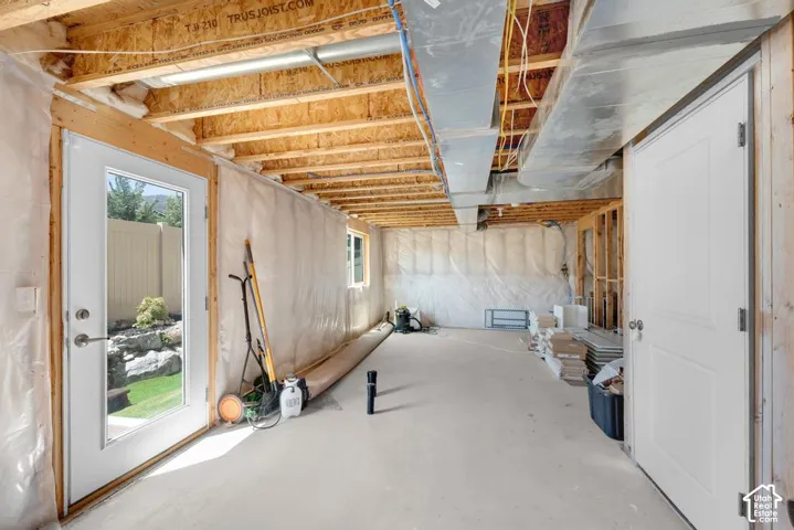 Unfinished basement featuring exposed joists, concrete flooring, exterior access, and a window