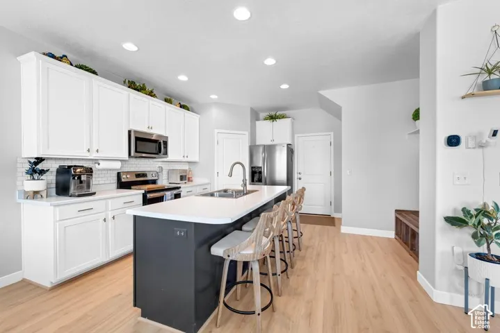 Kitchen featuring white shaker cabinetry, stainless steel appliances, a subway tile backsplash, a dark-toned island with a white countertop, and wood-finish flooring