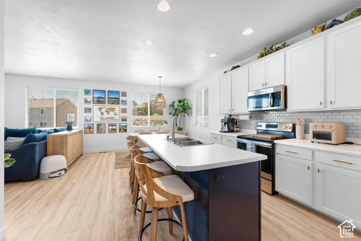 Kitchen featuring a large central island with seating, white shaker-style cabinetry, stainless steel appliances, and a subway tile backsplash