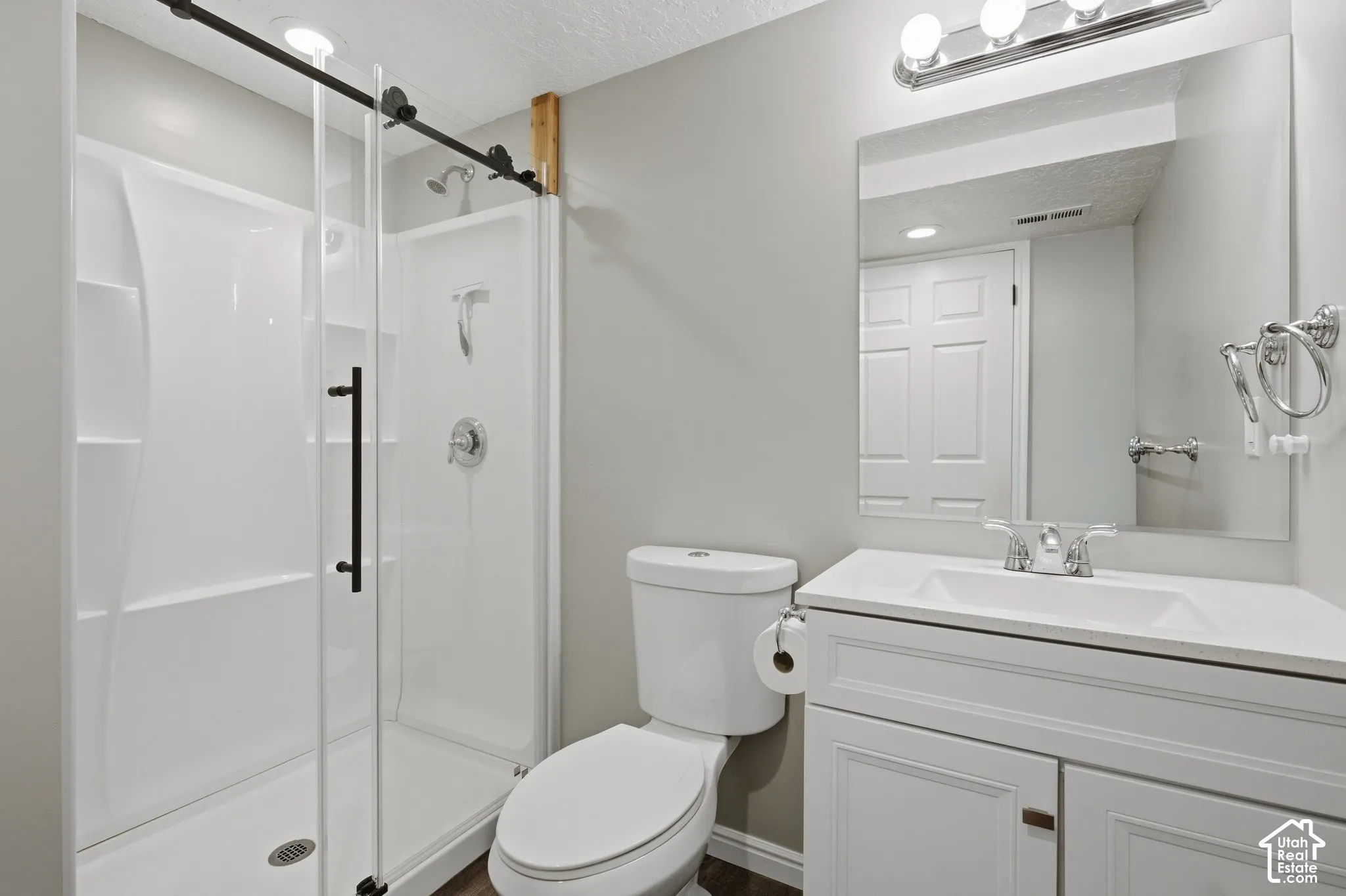White vanity with recessed paneling and chrome hardware, a white countertop with an integrated sink, a rectangular mirror, and a chrome light fixture with three bulbs