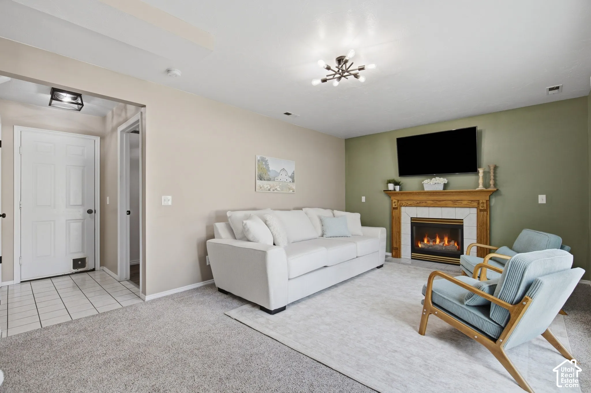 Carpeted flooring, wood-finish mantel, tiled fireplace surround, and a ceiling-mounted light fixture