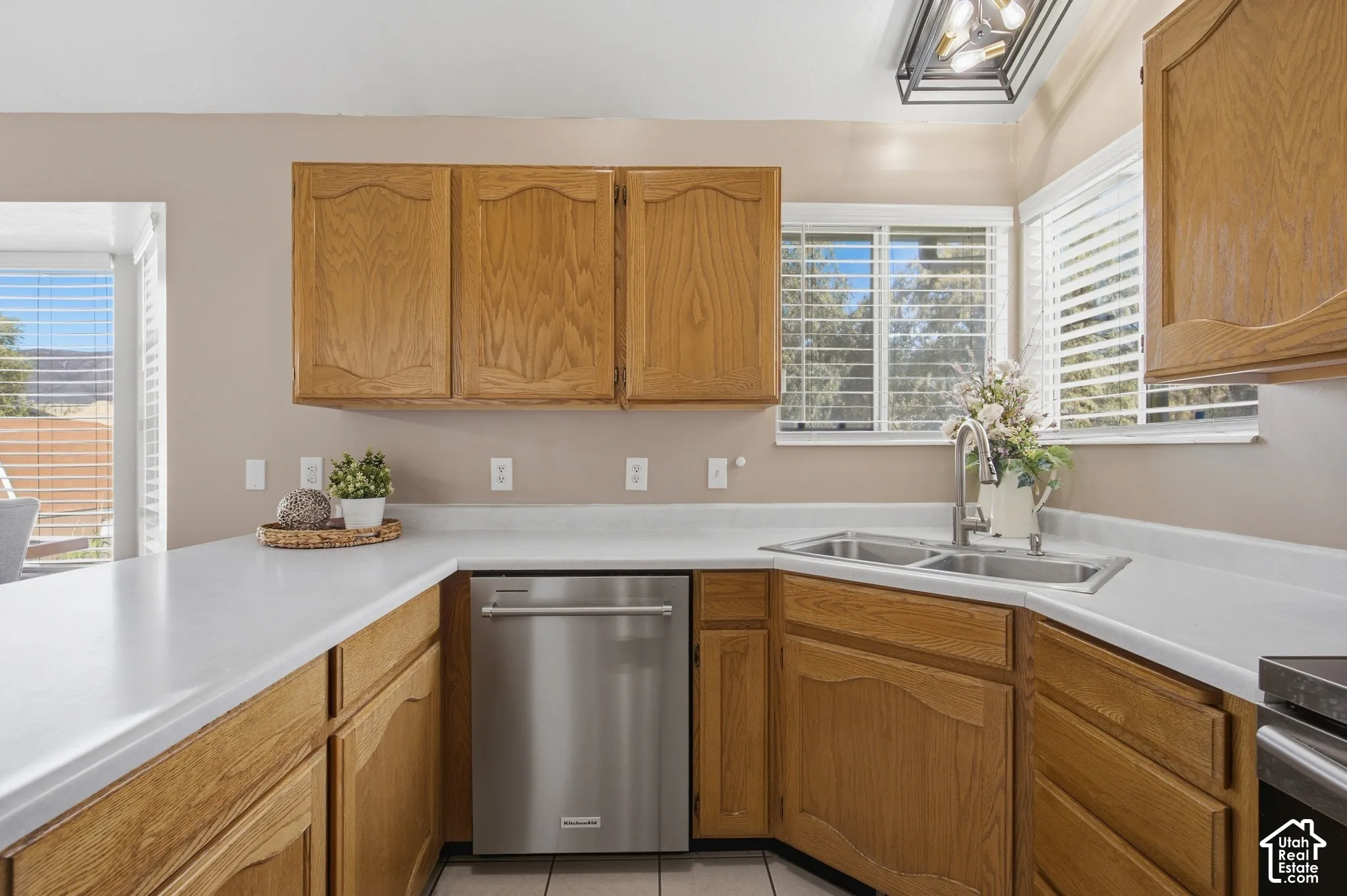 Kitchen featuring wood cabinetry, white countertops, a stainless steel dishwasher, and a double basin sink with a chrome faucet