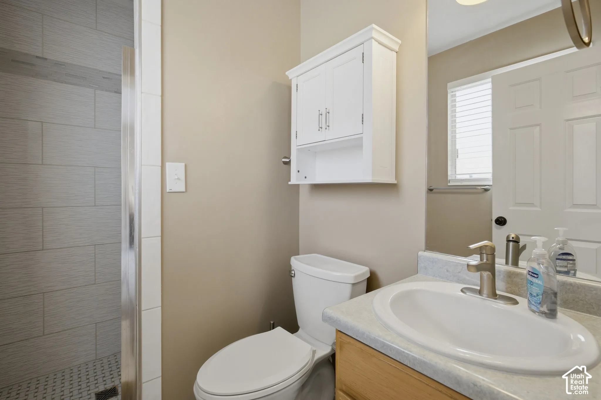 Tiled shower with glass enclosure, wood-finish vanity with an integrated sink, white wall-mounted cabinet, and a mirror