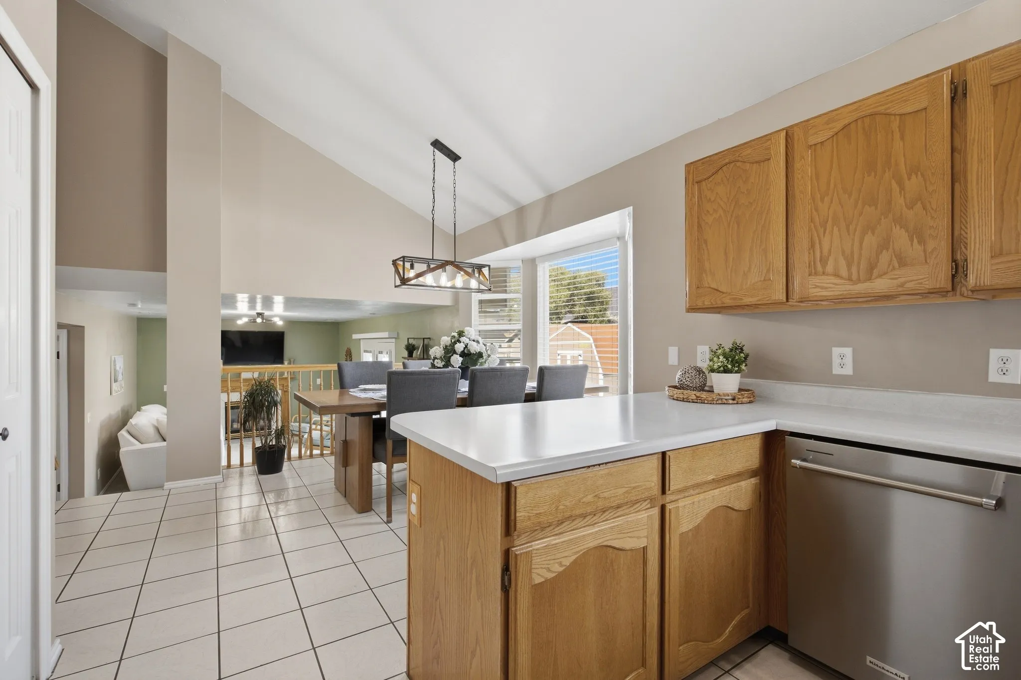 Kitchen and dining area featuring vaulted ceilings, wood-finish cabinetry, a stainless steel dishwasher, white countertops, and tile flooring