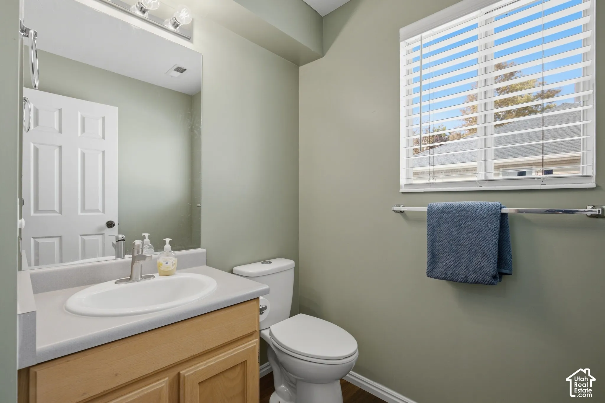 Vanity with an integrated sink, a window with horizontal blinds, and wood-finish flooring