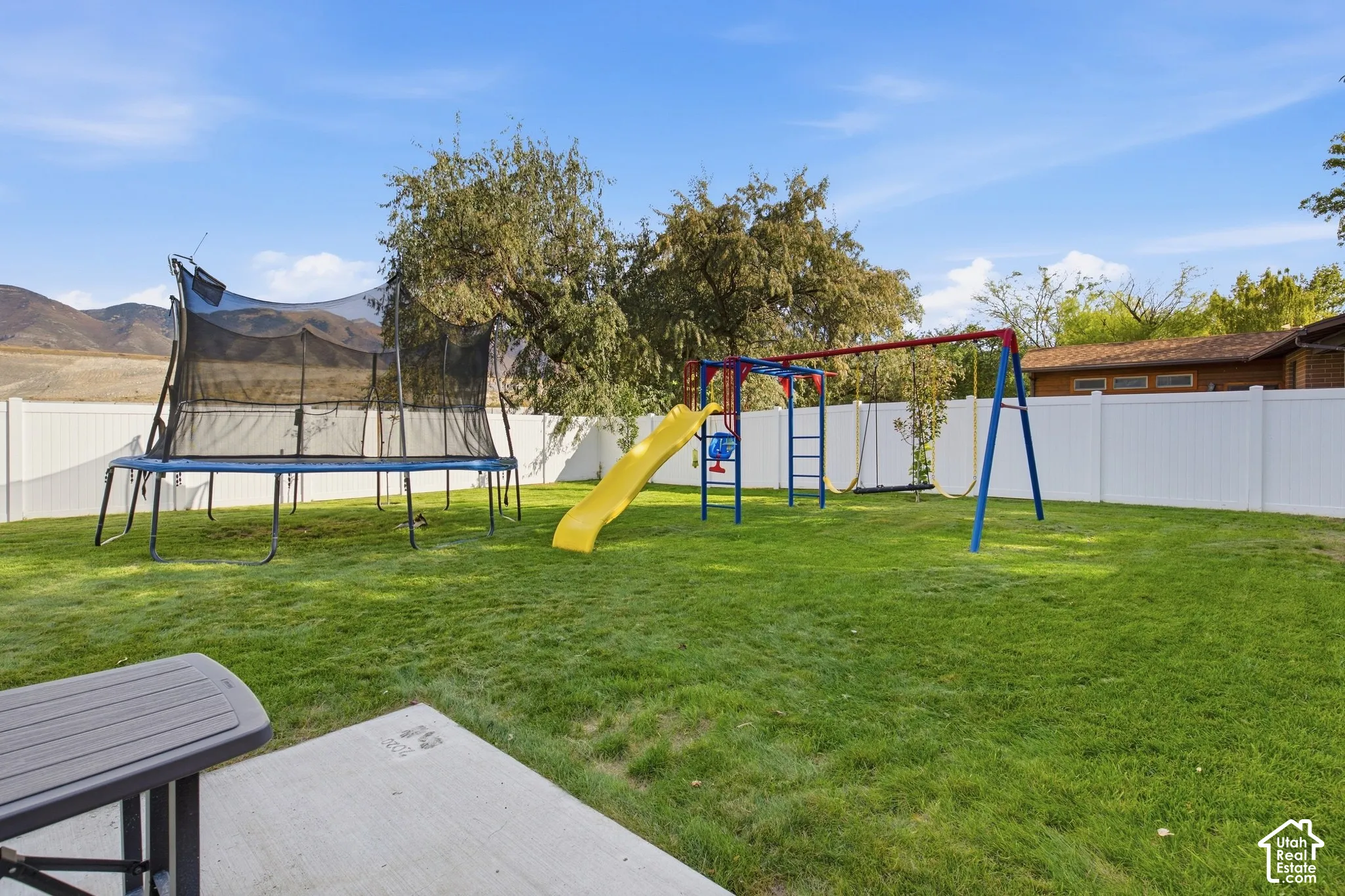 Spacious backyard oasis featuring a level lawn, mature shade trees, and a comprehensive play structure with slide and swings