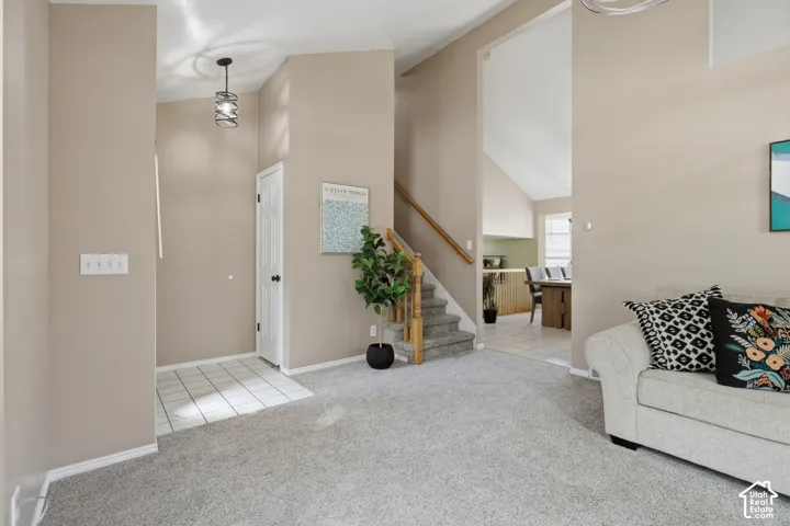 Vaulted entryway with tile flooring, staircase with wood handrail, and carpeted living area