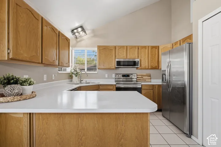 Vaulted ceiling kitchen featuring wood-finish cabinetry, white countertops, stainless steel appliances, and tiled flooring