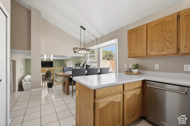 Kitchen and dining area featuring vaulted ceilings, wood-finish cabinetry, a stainless steel dishwasher, white countertops, and tile flooring