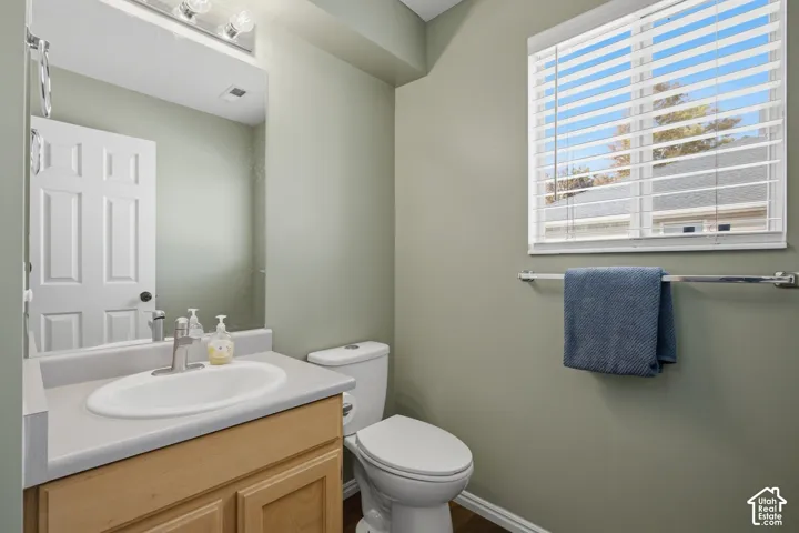 Vanity with an integrated sink, a window with horizontal blinds, and wood-finish flooring