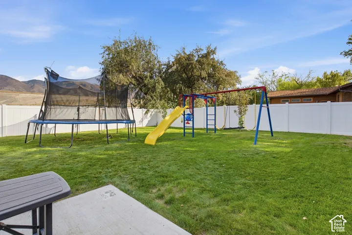 Spacious backyard oasis featuring a level lawn, mature shade trees, and a comprehensive play structure with slide and swings
