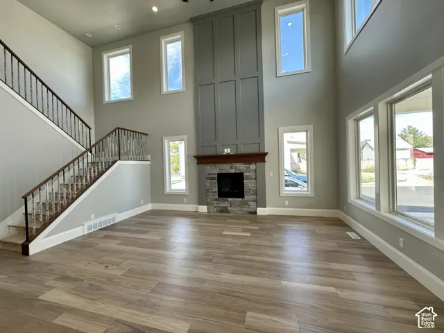 Two-story living area with wood-finish flooring, stone-clad fireplace with wood mantel, multiple large windows, and a staircase with wood handrails and metal balusters