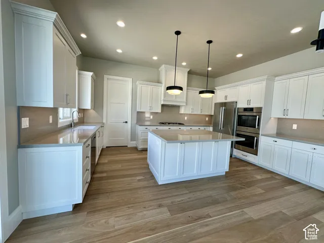 Light-toned wood-finish flooring, white cabinetry, integrated stainless steel appliances, a center island with pendant lighting, and recessed ceiling lights