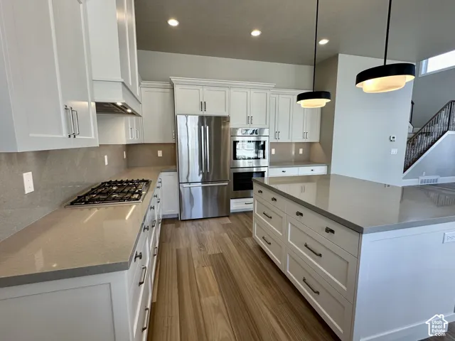 White cabinetry with brushed nickel hardware, light-toned countertops, wood-finish flooring, stainless steel appliances, and island with integrated storage