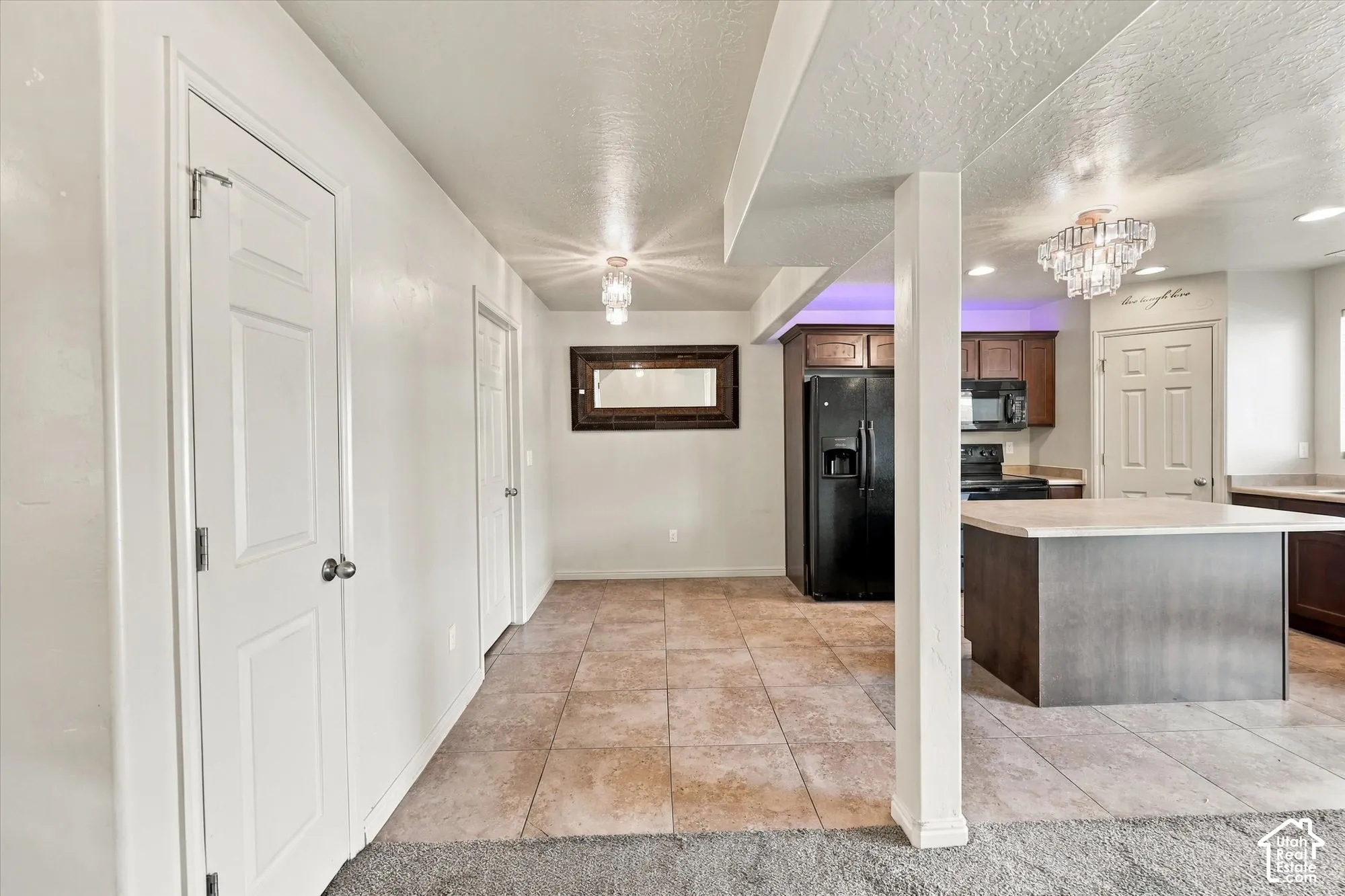 Kitchen featuring dark wood-finish cabinetry, black appliances, a central island with a light-toned countertop, and recessed lighting