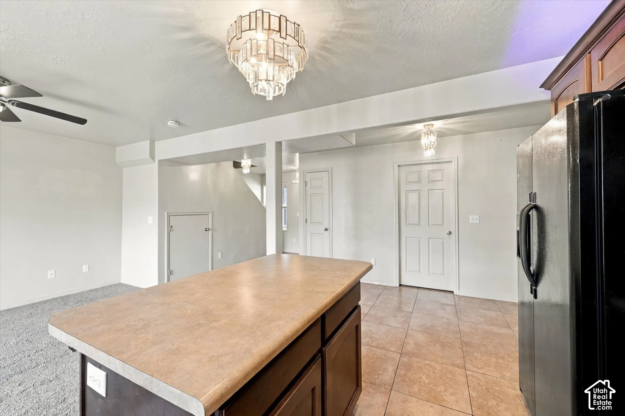 Kitchen island with a light-colored countertop and dark wood-finish cabinetry, tile flooring, and a black refrigerator