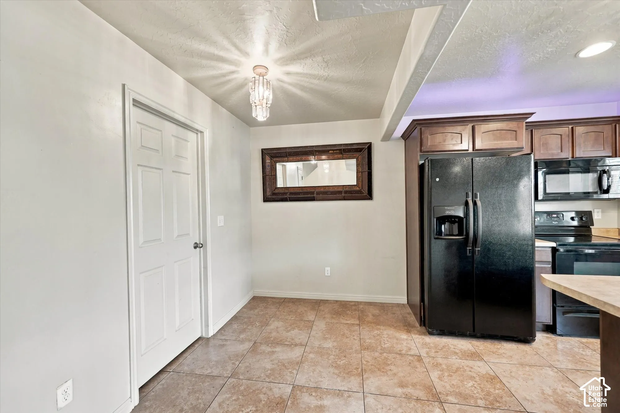 Kitchen area with tile flooring, built-in cabinetry, and a black side-by-side refrigerator