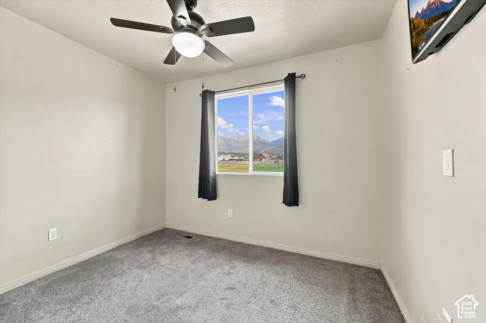 Gray carpeted flooring, a window offering mountain scenery, a ceiling fan with integrated lighting, and neutral wall tones