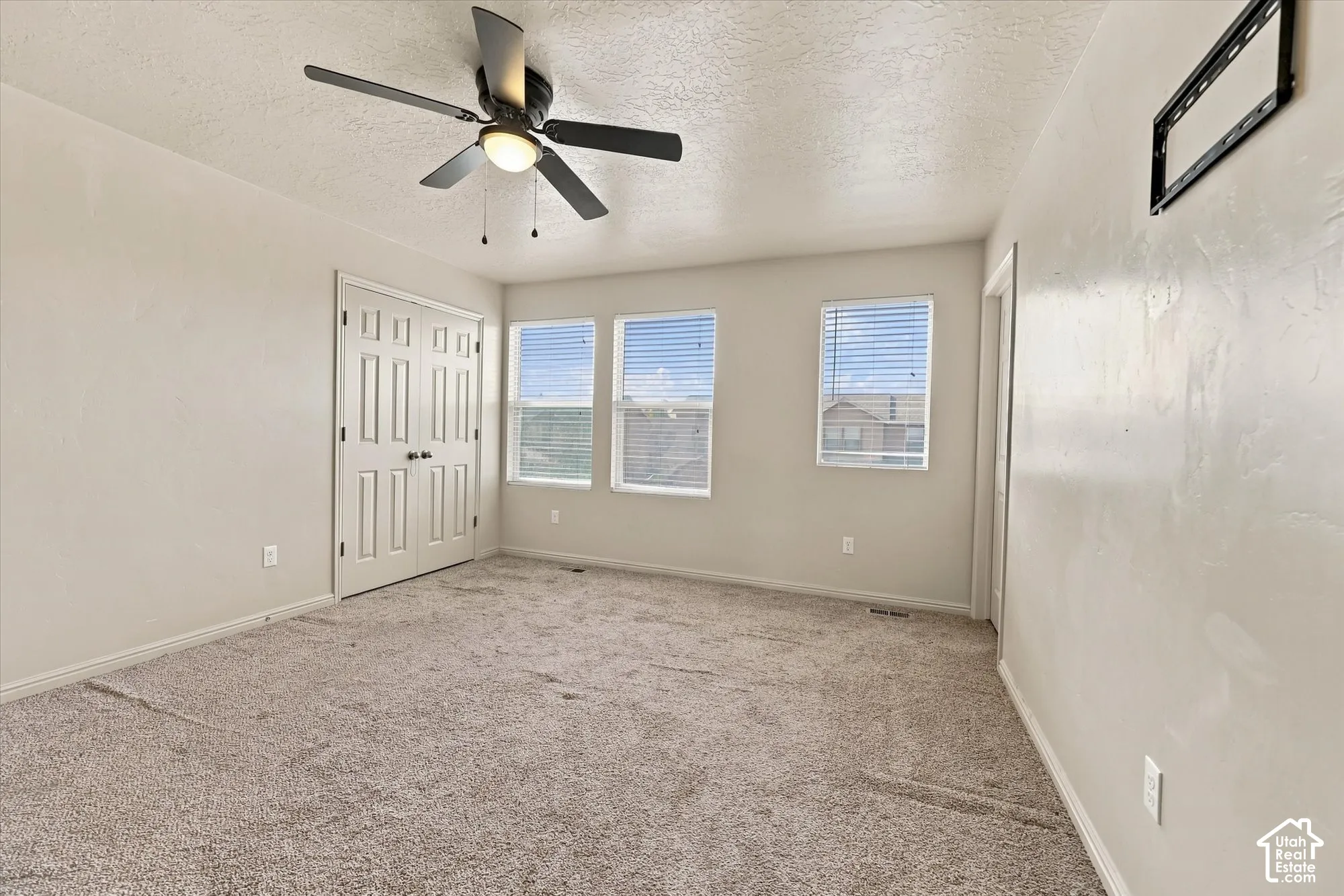 Neutral tone walls, plush carpeting, ceiling fan with integrated lighting, multiple windows with blinds, and paneled bifold closet doors
