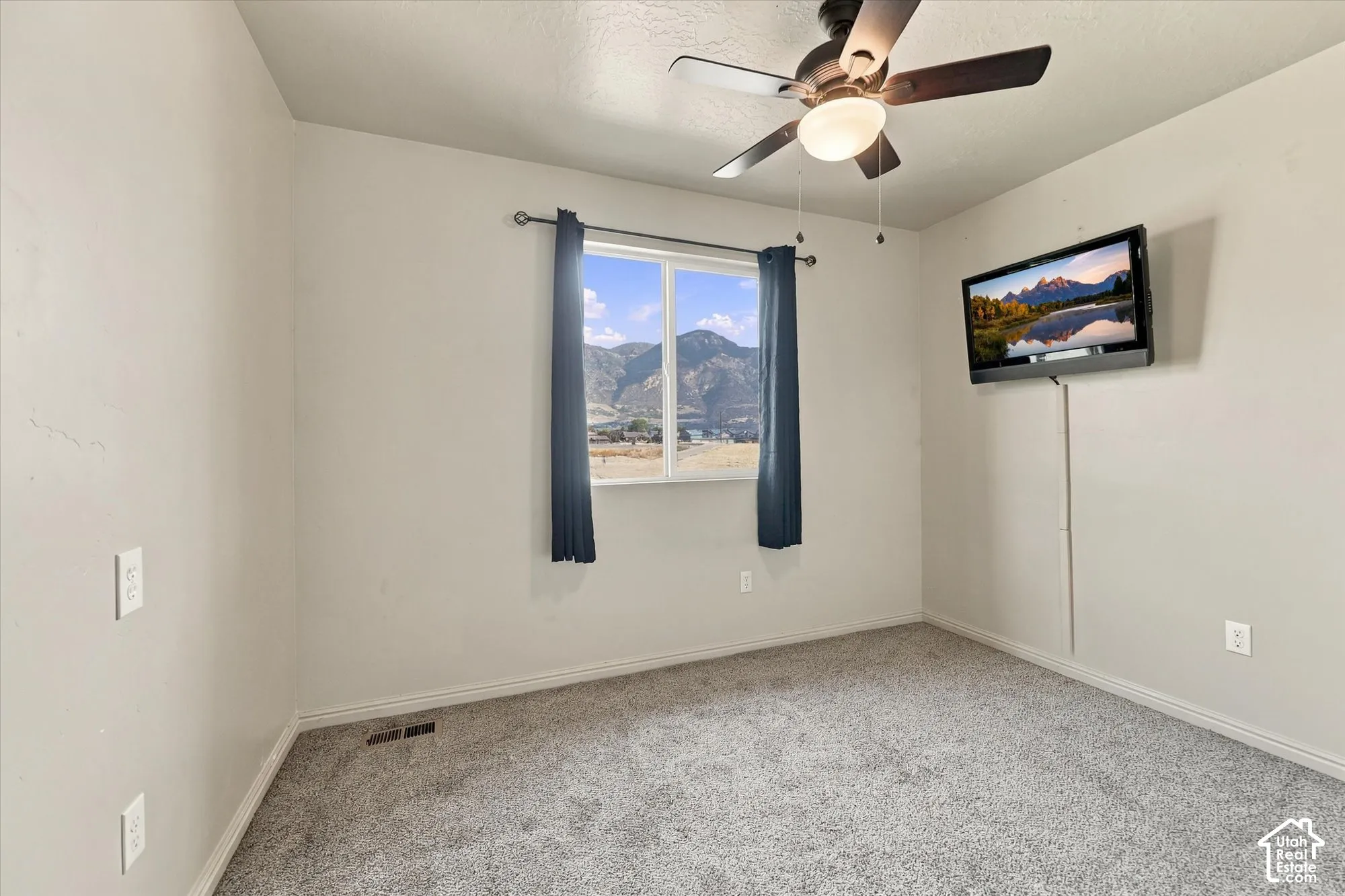 Carpeted room featuring a ceiling fan with integrated lighting, a window with curtains, and wall-mounted electrical outlets