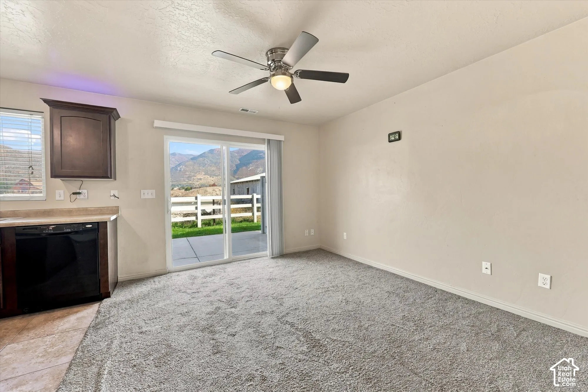 Sliding glass door, kitchen cabinetry, built-in dishwasher, ceiling fan, and mountain backdrop
