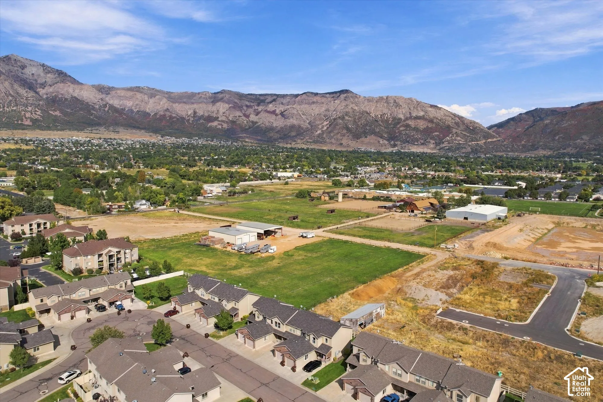 Expansive undeveloped land with mountain backdrop, surrounding residential developments, and new road infrastructure