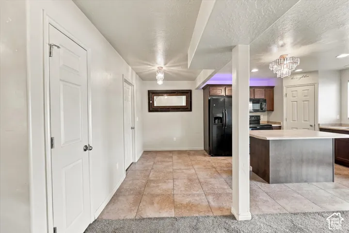 Kitchen featuring dark wood-finish cabinetry, black appliances, a central island with a light-toned countertop, and recessed lighting