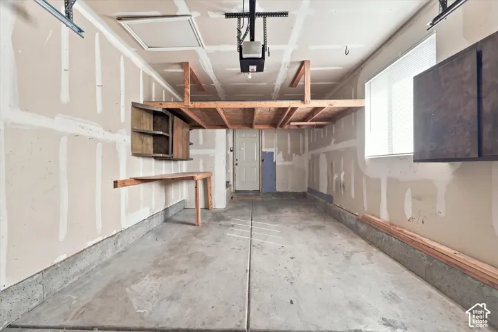 Attached garage with concrete flooring, overhead storage platform, built-in cabinetry, and a single window with blinds