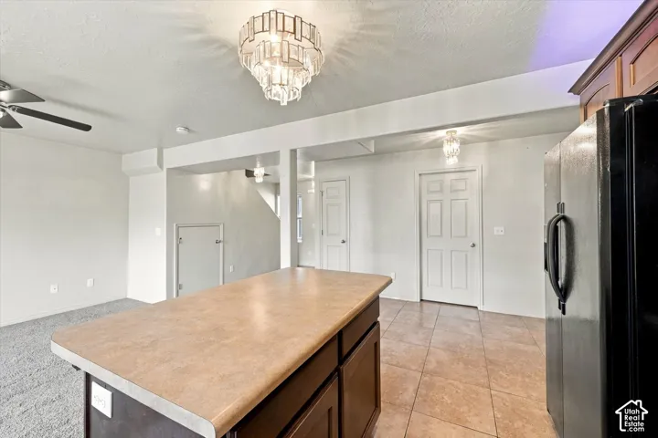 Kitchen island with a light-colored countertop and dark wood-finish cabinetry, tile flooring, and a black refrigerator