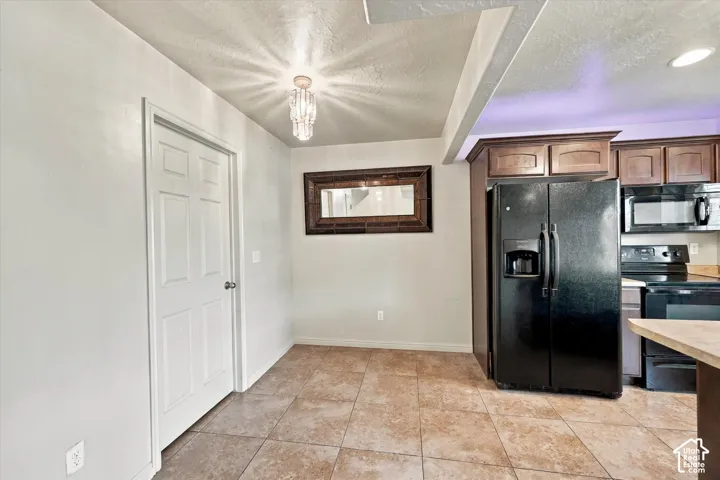 Kitchen area with tile flooring, built-in cabinetry, and a black side-by-side refrigerator