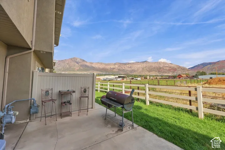 Paved patio with mountain backdrop, bordered by a white rail fence and green space