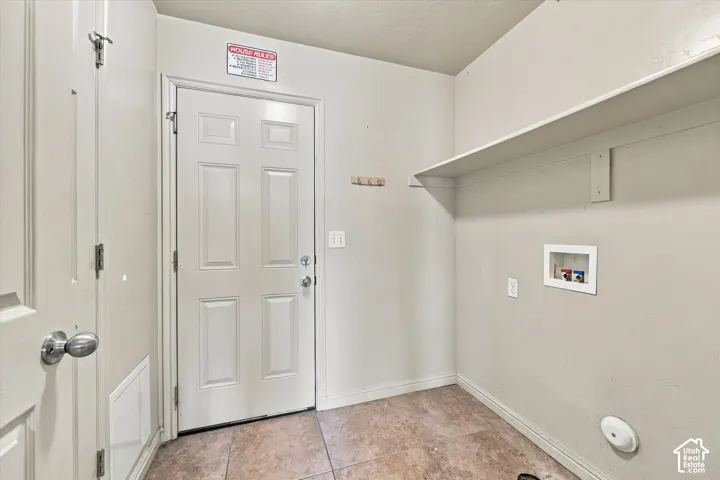 Laundry area featuring tile flooring, a utility door, and a built-in storage shelf