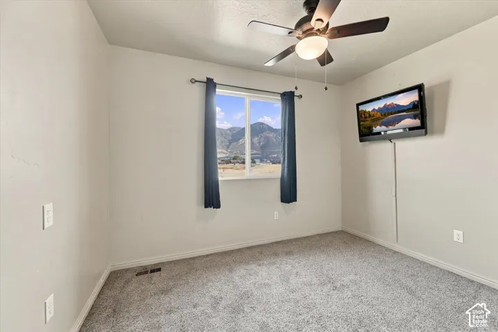 Carpeted room featuring a ceiling fan with integrated lighting, a window with curtains, and wall-mounted electrical outlets
