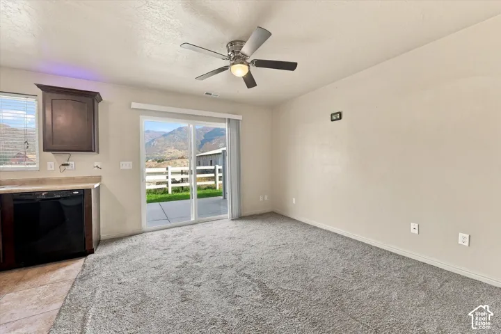 Sliding glass door, kitchen cabinetry, built-in dishwasher, ceiling fan, and mountain backdrop