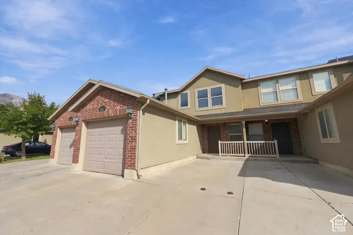 Exterior featuring brick and stucco siding, multiple windows, two garage doors, and a covered entry with a white railing