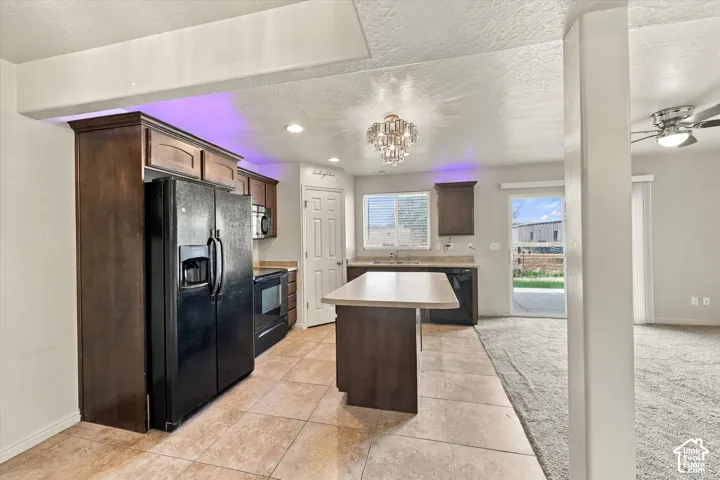 Kitchen featuring dark wood-finish cabinetry, black appliances, a central island, and tile flooring