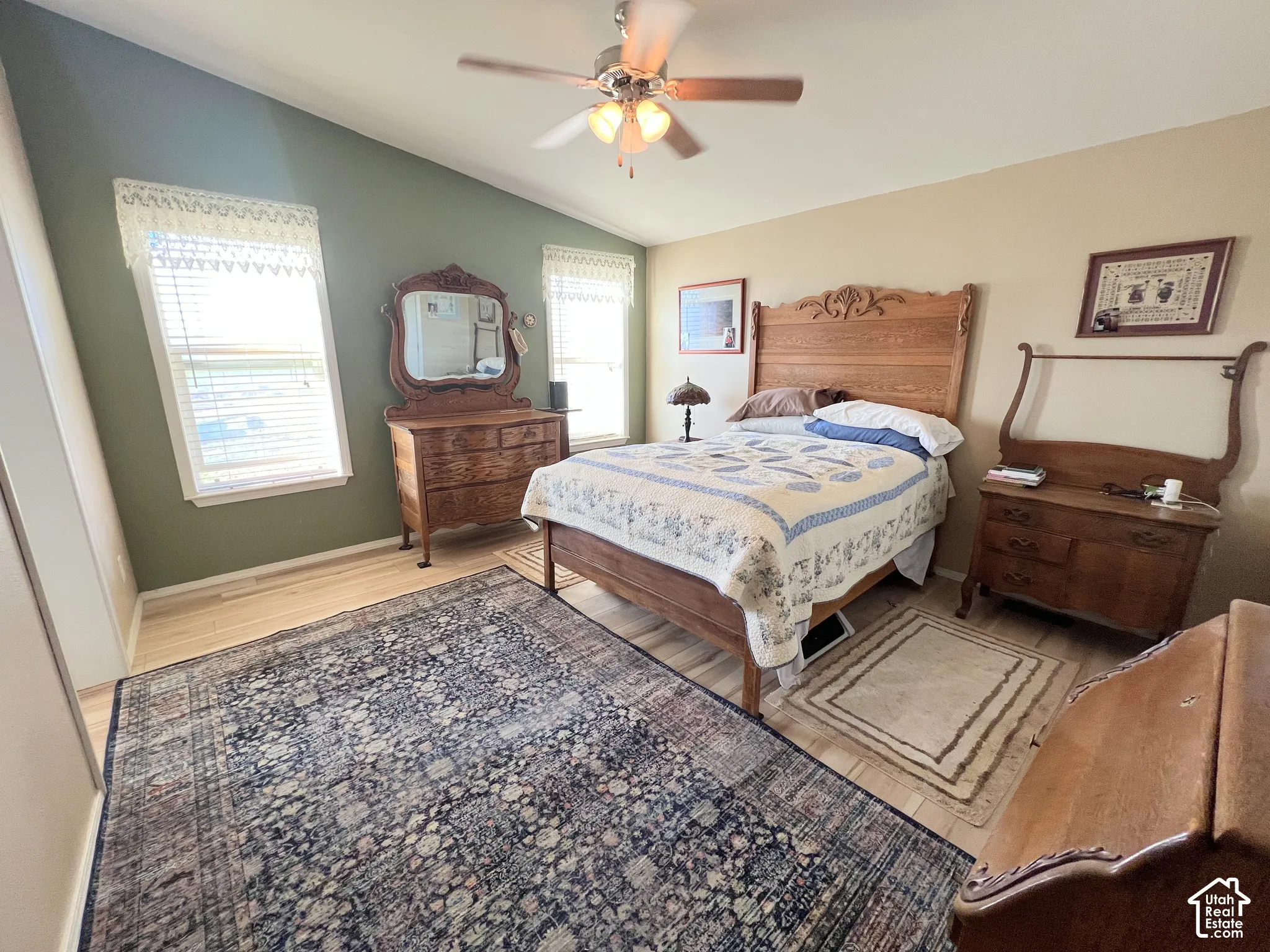 Vaulted ceiling, two windows with blinds, wood-finish flooring, and a ceiling fan with integrated lighting