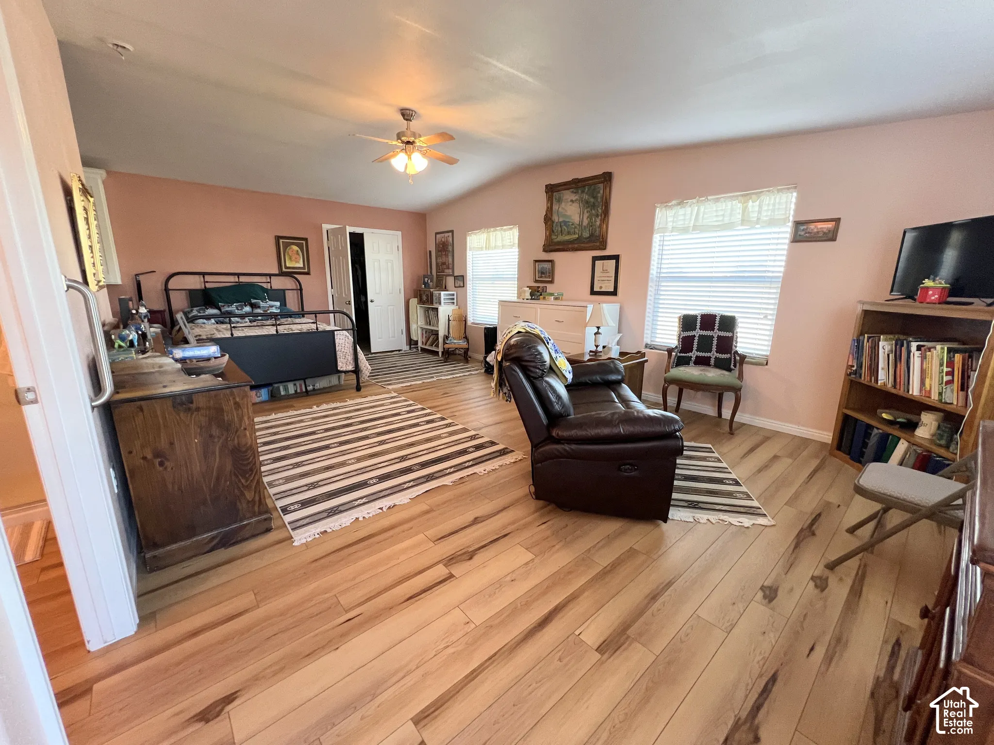 Wood-finish flooring throughout, vaulted ceiling with a ceiling fan, and multiple windows with blinds