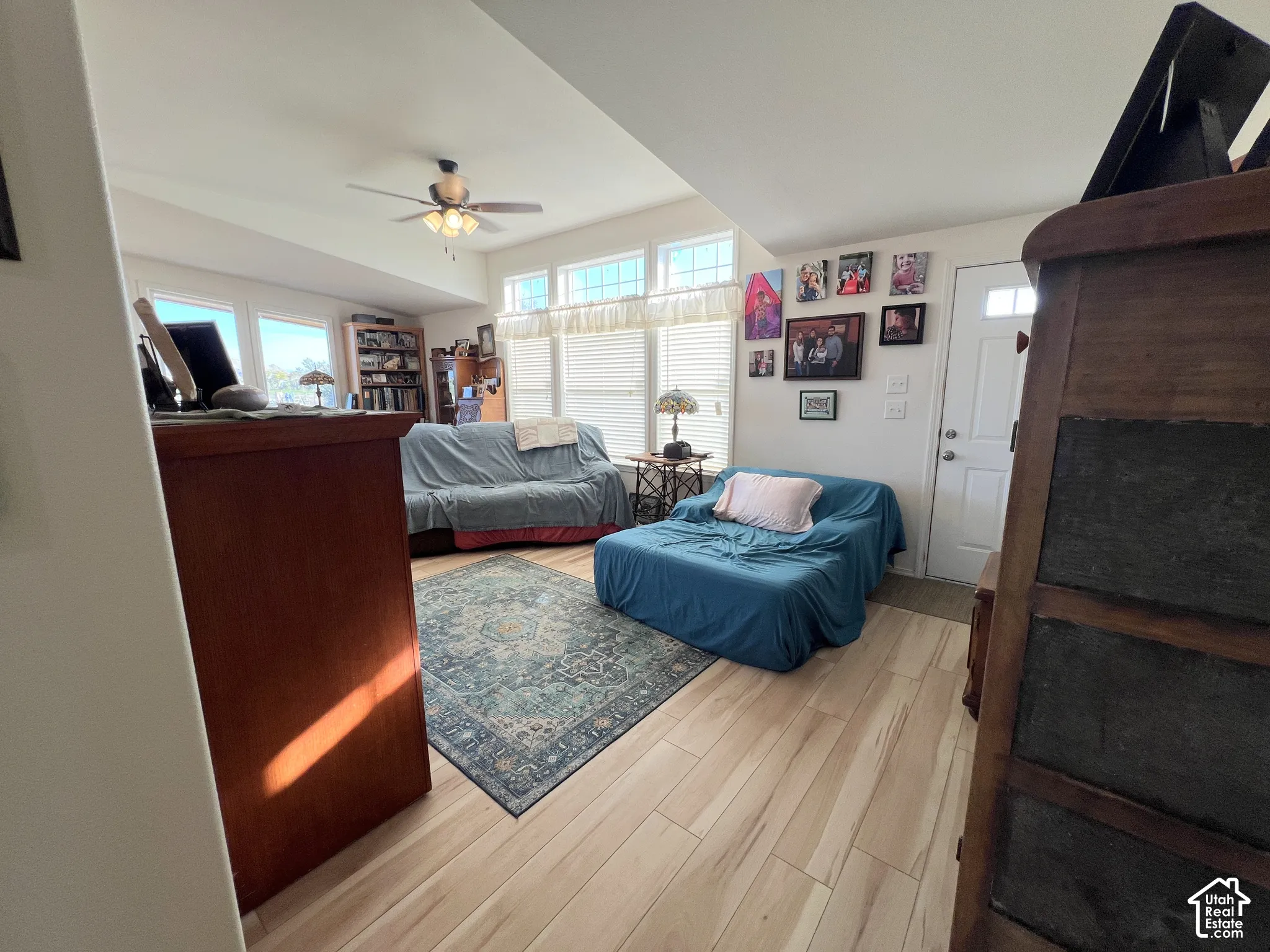 Wood-finish flooring throughout, ceiling fan with integrated lighting, and multiple windows with horizontal blinds