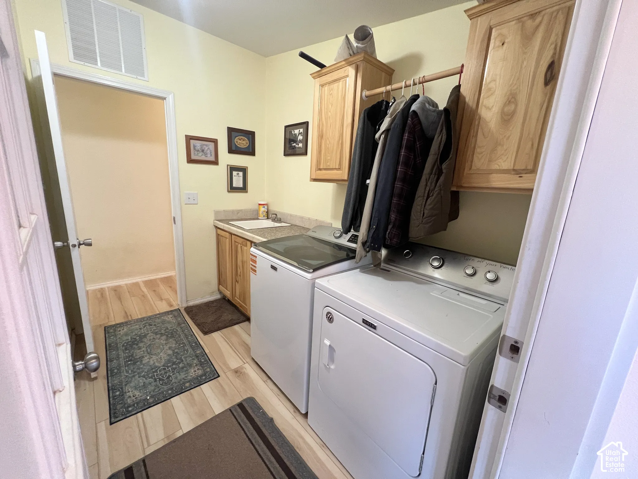 Utility room featuring wood-finish flooring, built-in cabinetry, a utility sink with a stone-finish countertop, and overhead storage