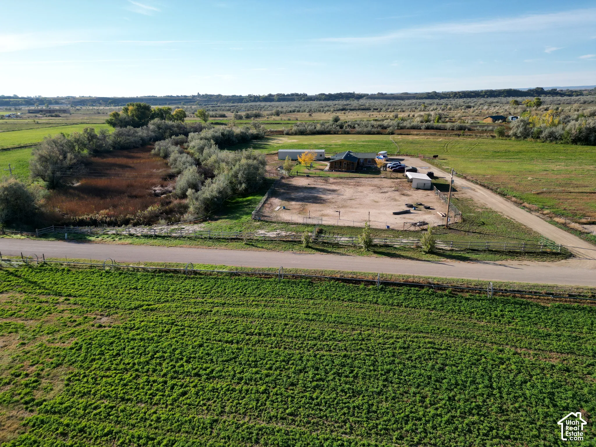 Expansive rural property featuring a wood-sided structure, surrounding green fields, natural water features, and a dirt road entrance