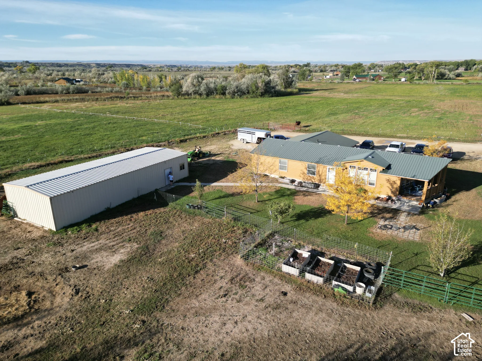 Single-story residence with a metal roof and light-colored siding, accompanied by a long, detached metal outbuilding