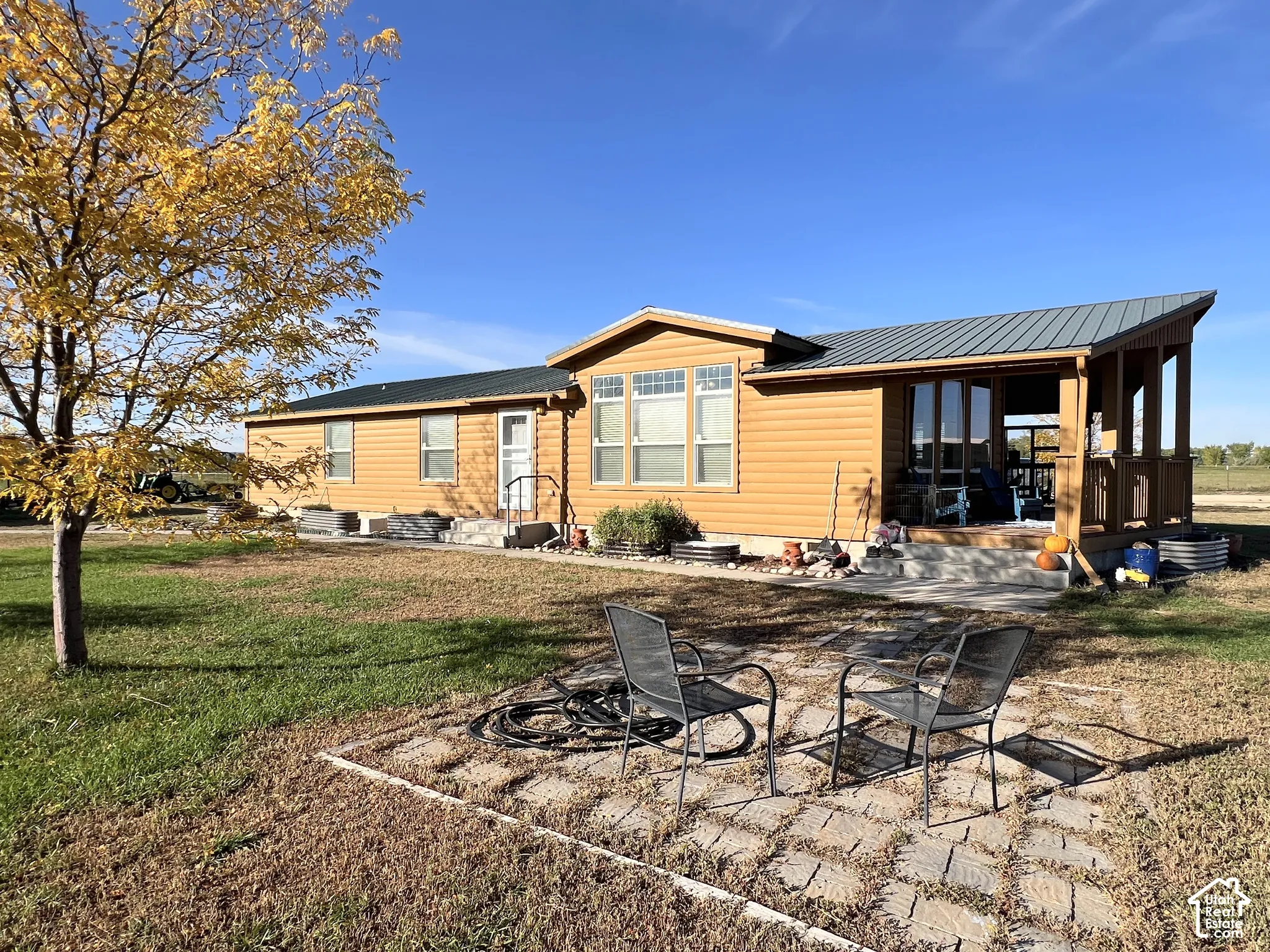 Exterior siding in a natural wood tone, covered porch with wood railing, metal roof, and a patterned paver patio