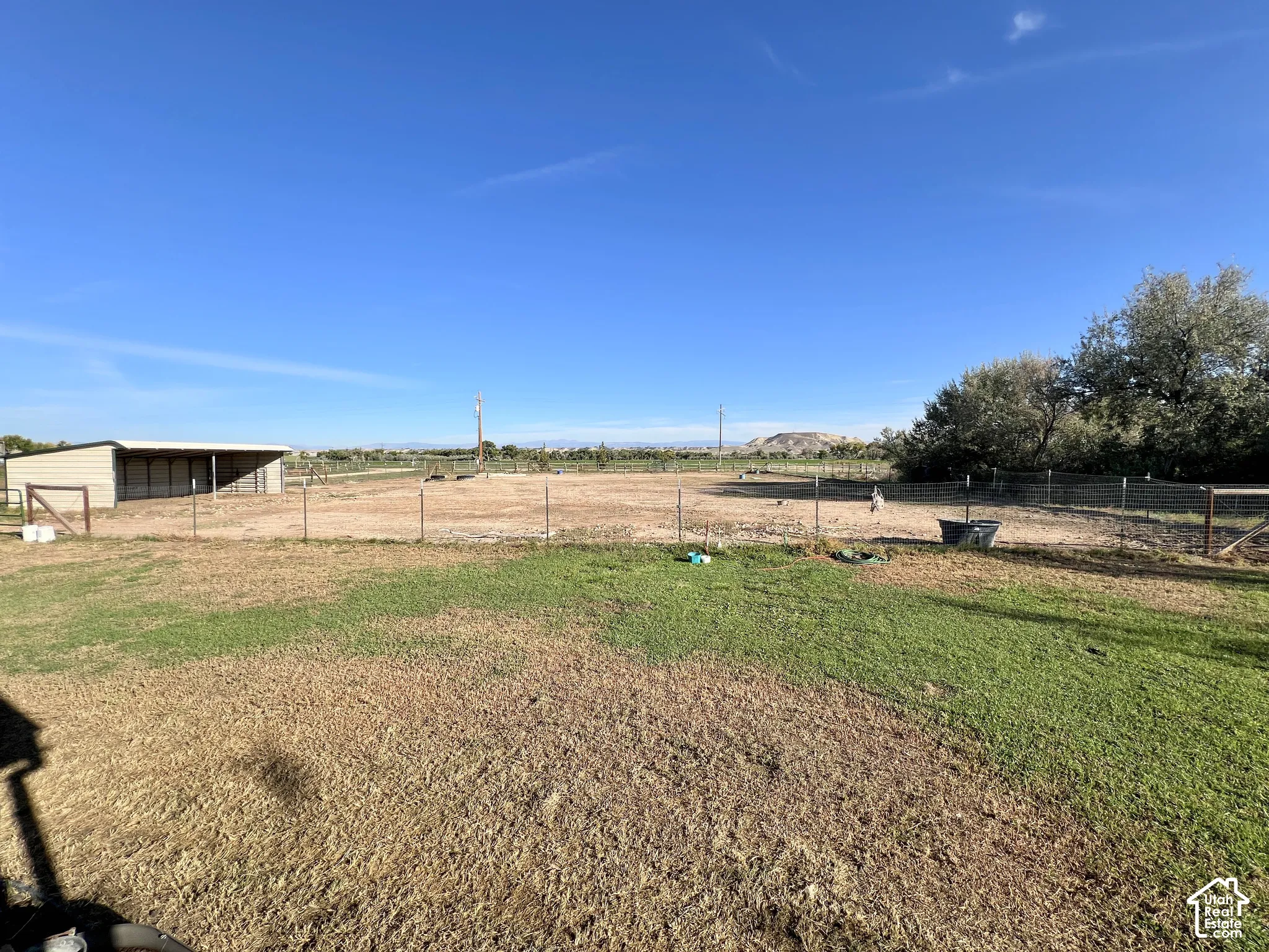 Expansive outdoor space featuring a covered animal shelter, fenced areas, and distant natural scenery
