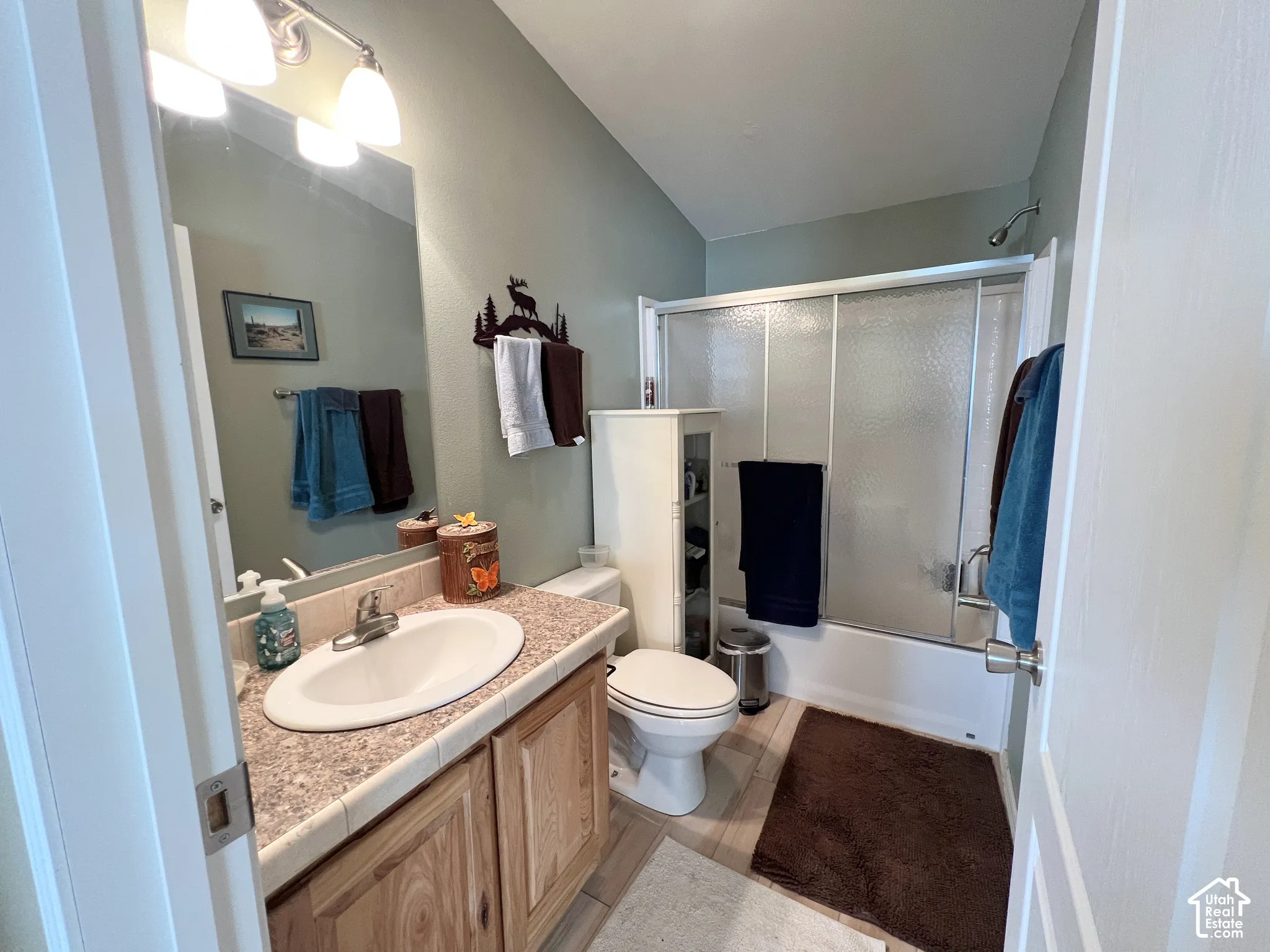 Vanity with wood-finish cabinetry, tile countertop, and an oval undermount sink