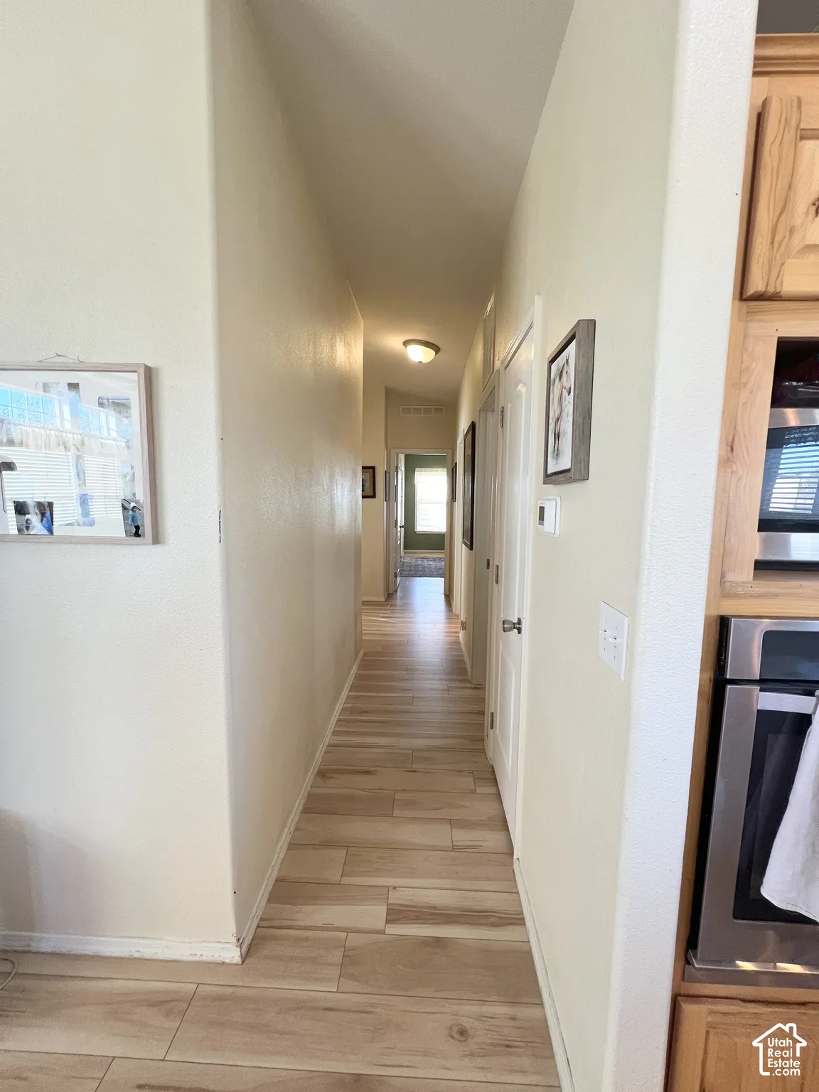 Wood-finish tile flooring throughout the hallway, featuring light-toned walls and built-in cabinetry with stainless steel appliances